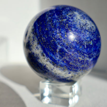 1.5-inch lapis lazuli crystal sphere with pyrite inclusions, showing deep indigo color and golden flecks on a white background.