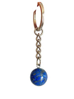 A close-up of a hand holding a silver keychain with a blue lapis lazuli sphere charm against a plain light gray background.