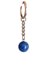 A close-up of a hand holding a silver keychain with a blue lapis lazuli sphere charm against a plain light gray background.