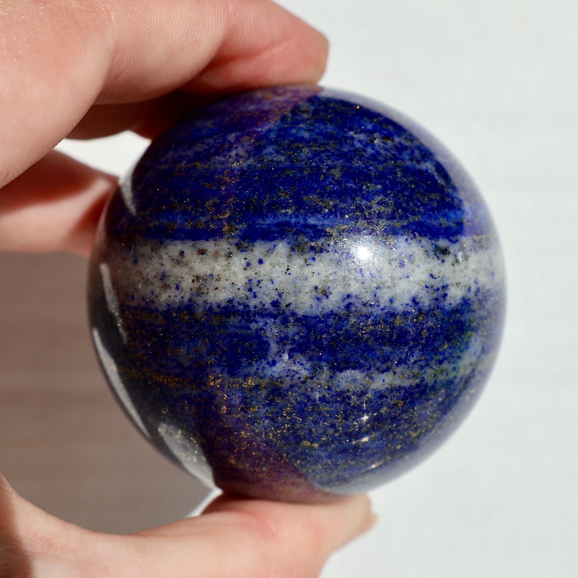 Small lapis lazuli sphere resting in an open palm, highlighting size and cool-to-the-touch polish.
