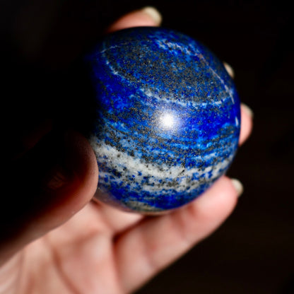 Small lapis lazuli sphere resting in an open palm, highlighting size and cool-to-the-touch polish.