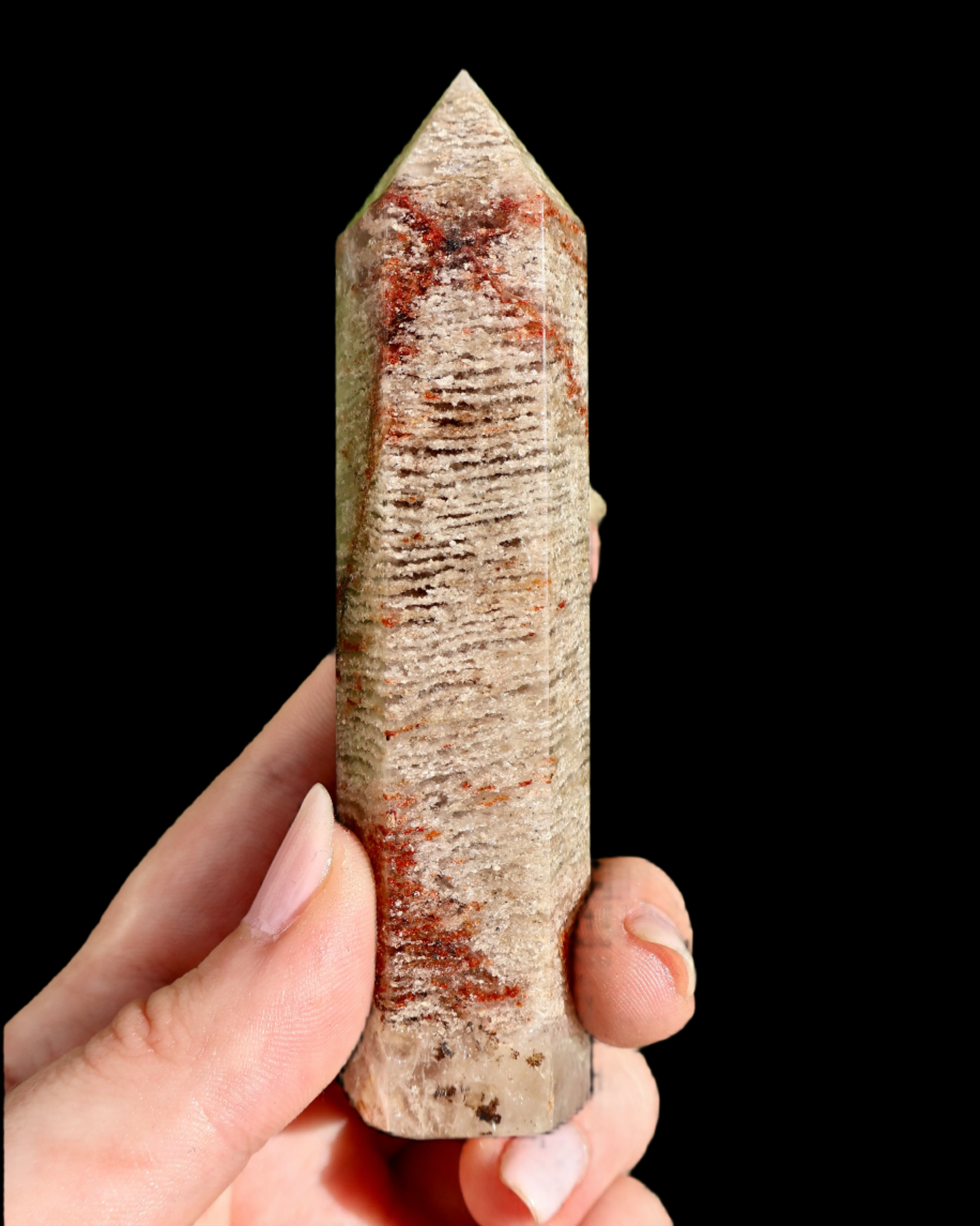 Hand holding a crystal with red veinings against a black background