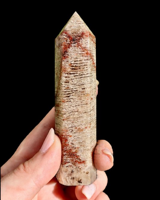 Hand holding a crystal with red veinings against a black background