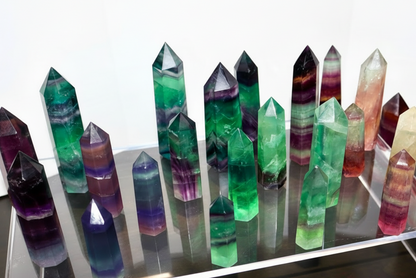 Colorful crystal formations on a reflective surface with smaller crystals on a wooden surface.