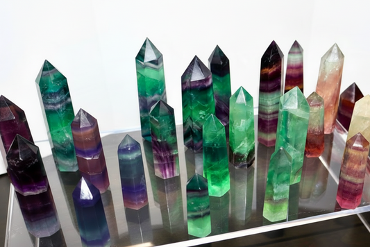 Colorful crystal formations on a reflective surface with smaller crystals on a wooden surface.