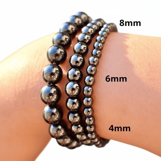 Three beaded stretch bracelets in different sizes (8mm, 6mm, and 4mm) worn on a wrist. The bracelets are made of polished black beads with a metallic sheen, reflecting the surrounding environment.